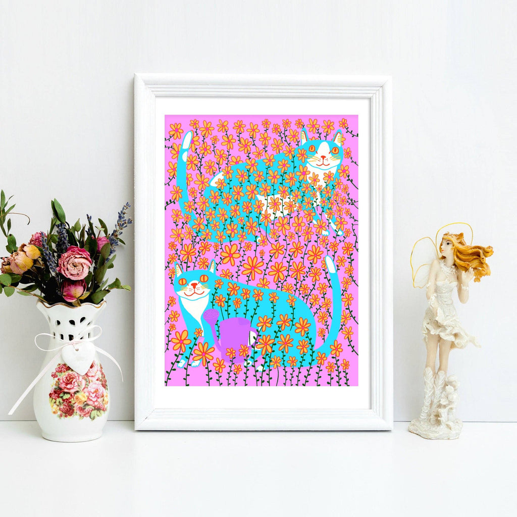 Framed artwork of cats among flowers on a white surface with decorative items.