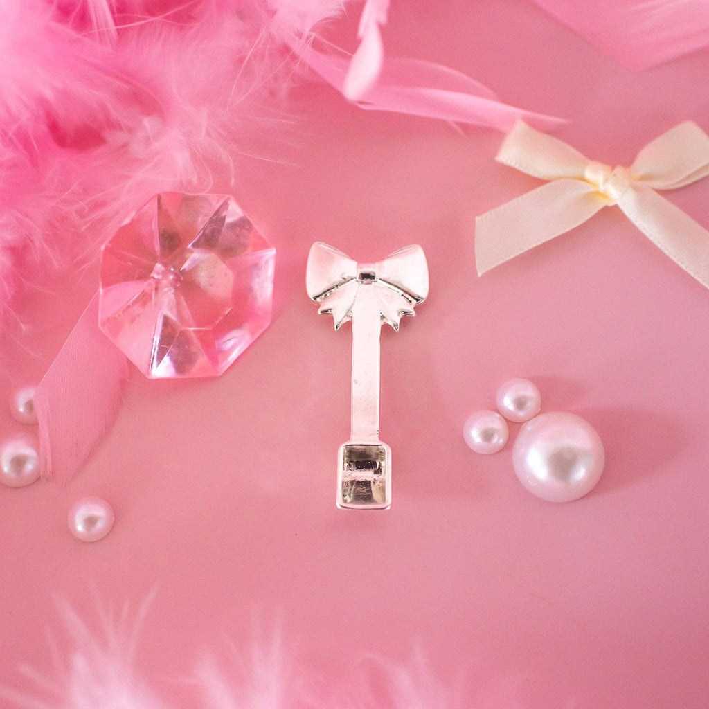 Key-shaped hair clip with bow on a pink background with feathers and crystals
