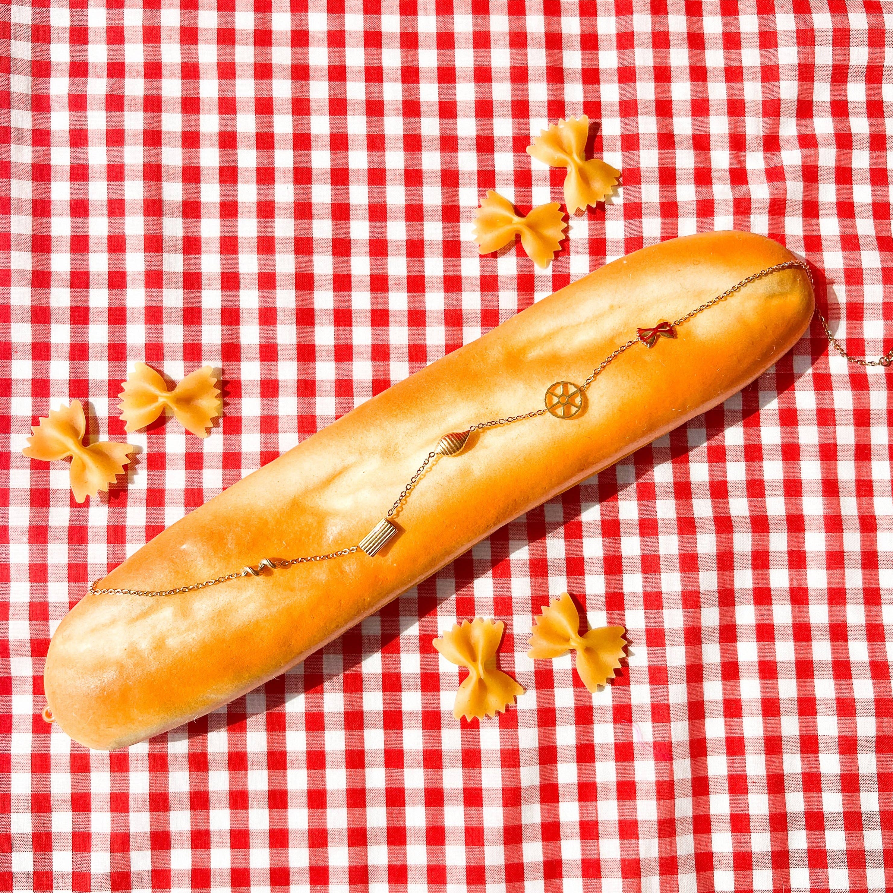 Long loaf of bread with a necklace on a red and white checkered tablecloth