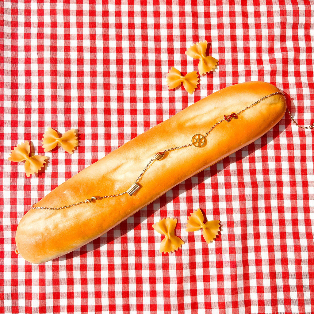 Long loaf of bread with a necklace on a red and white checkered tablecloth