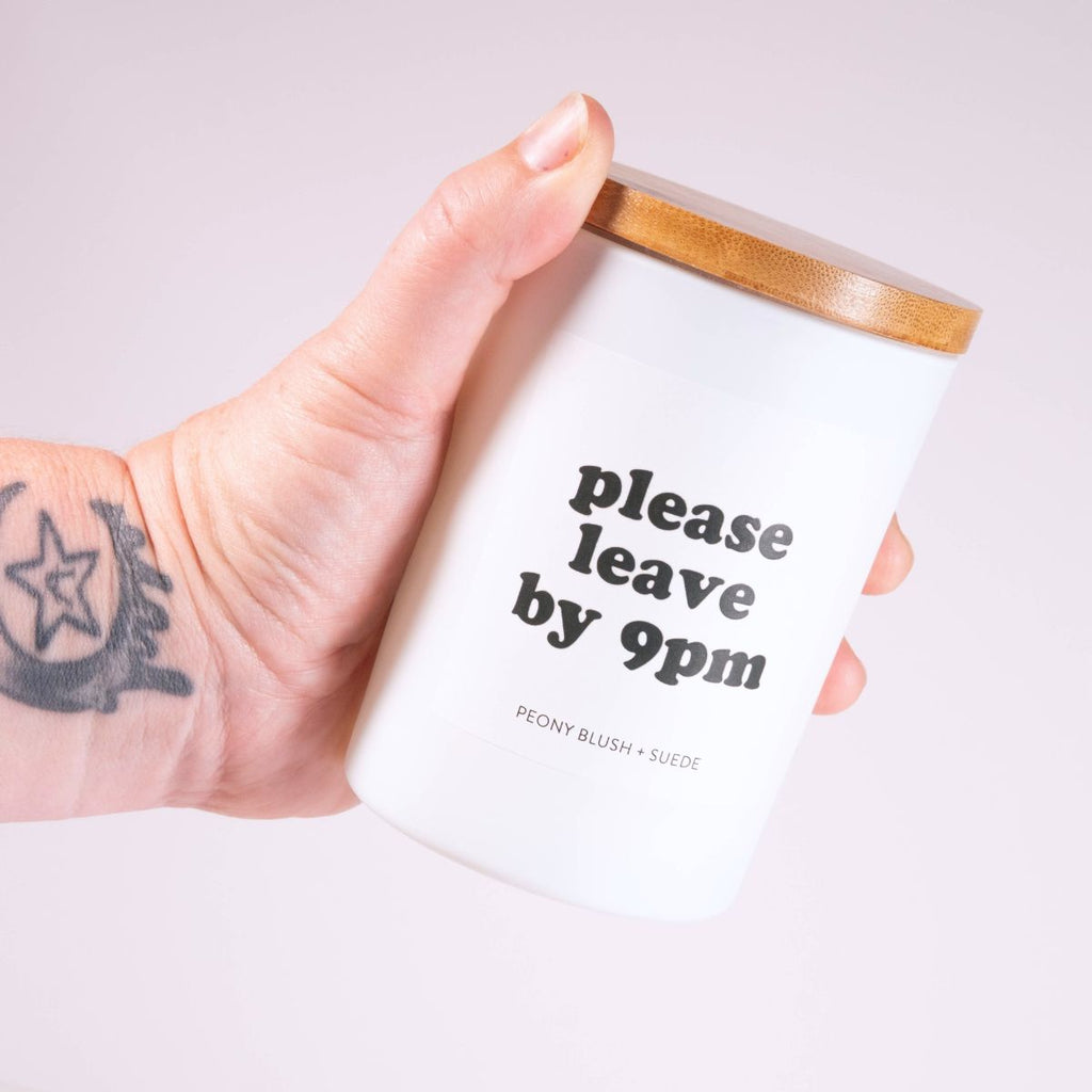 Hand holding a white candle with 'please leave by 9pm' text on a light gray background