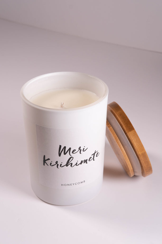 White candle in a glass container with a wooden lid on a light gray background