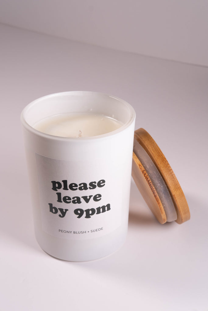 White candle in a glass jar with a wooden lid on a light gray background