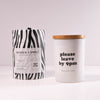 Candle with zebra-patterned lid and white candle with wooden lid on a light background