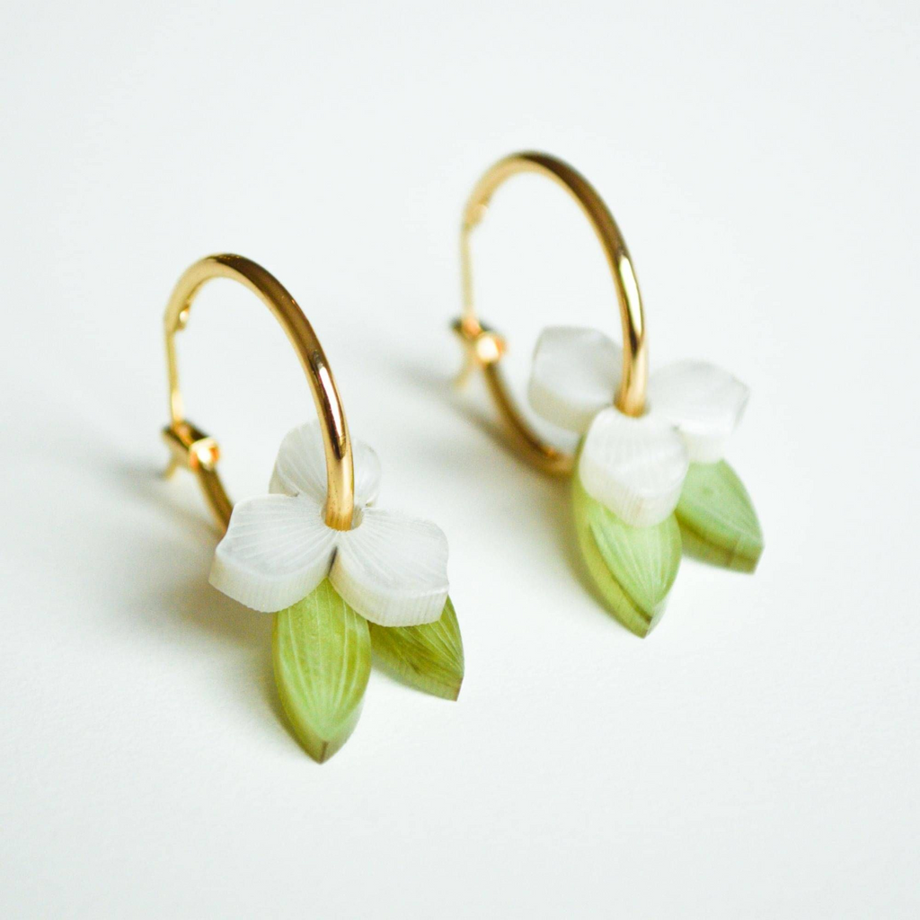 Gold hoop earrings with white floral and green leaf details on a light background