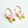 Gold hoop earrings with pink floral and green leaf details on a white background