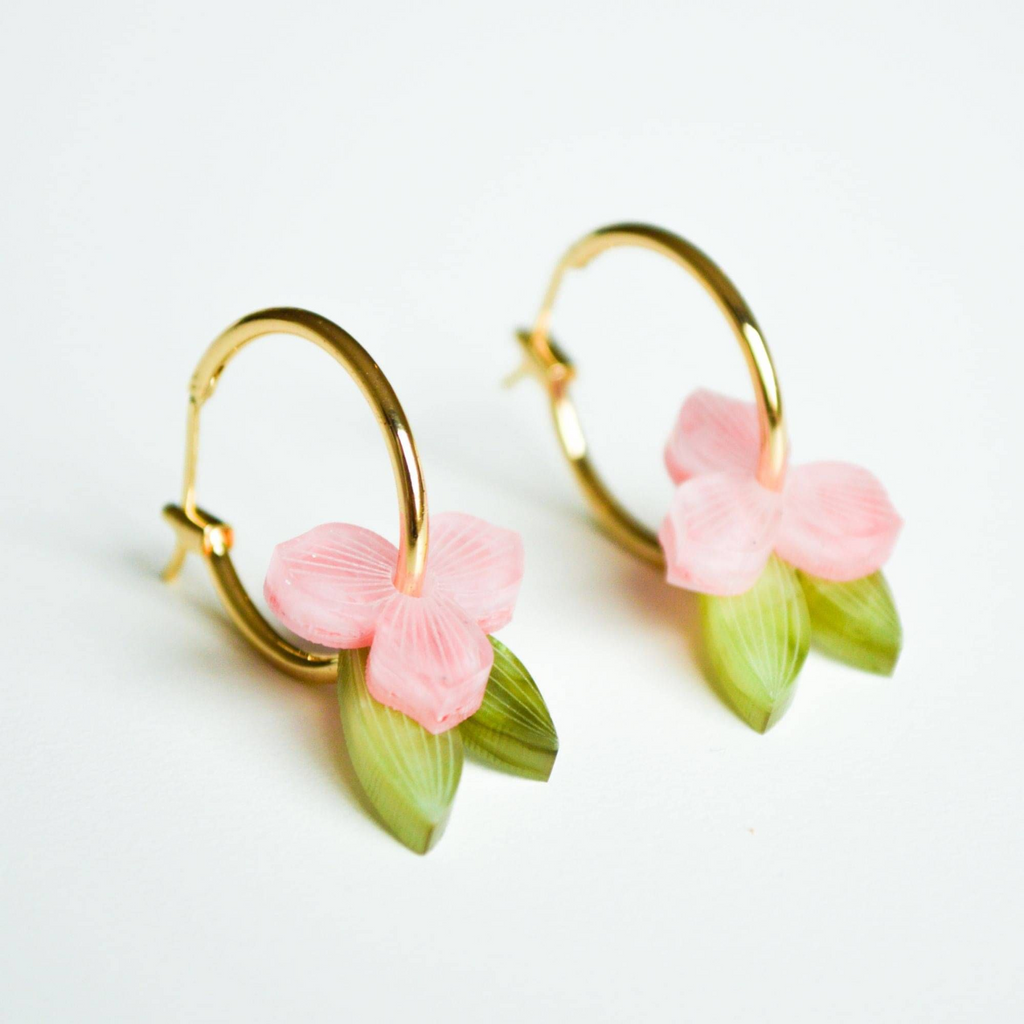 Gold hoop earrings with pink floral and green leaf details on a white background