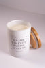Candle in a white container with text and a wooden lid on a light gray background