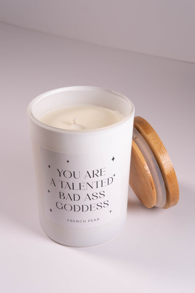 Candle in a white container with text and a wooden lid on a light gray background