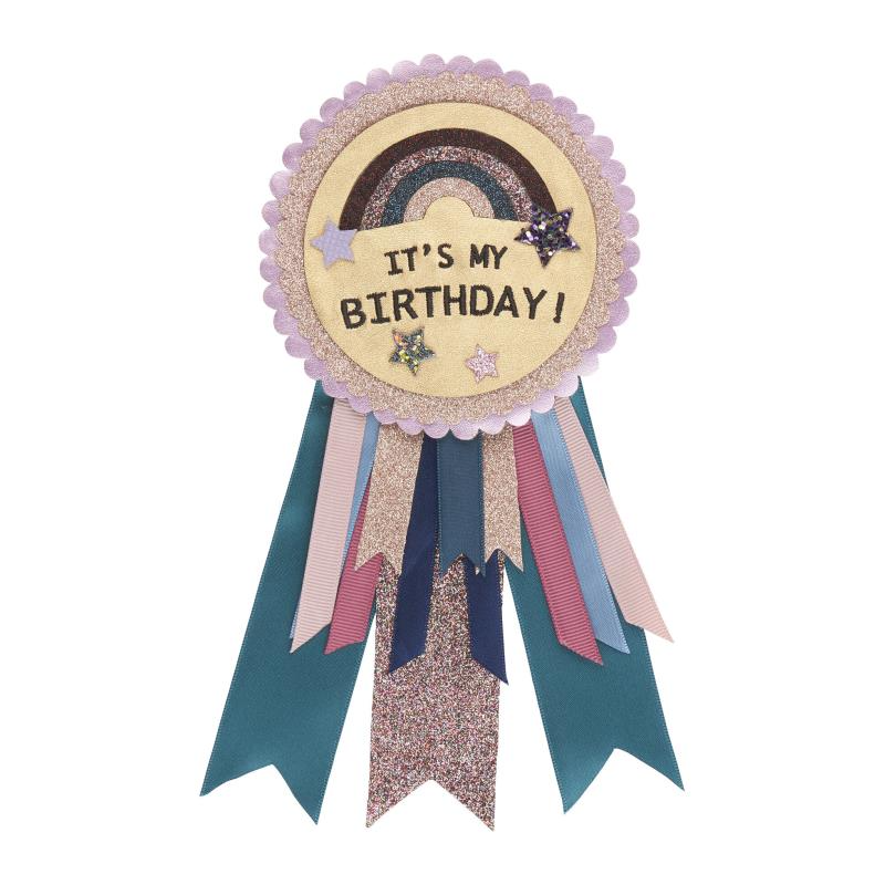A birthday rosette with a unicorn and rainbow design, featuring layers of scalloped trim, glitter, and metallic leatherette fabric with satin, grosgrain, and glitter ribbons.